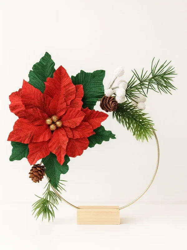 Håndlavet juledekoration med papir-julestjerne i crepepapir, grønne blade, kogler og vintergrene på en metalring med træfod, egnet til både vægophæng og stående dekoration.