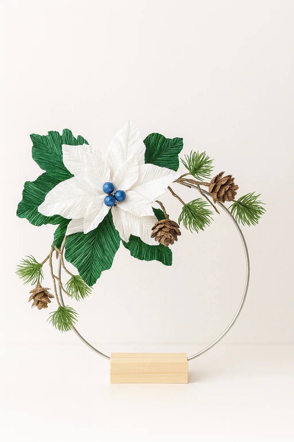 Håndlavet juledekoration med papir-julestjerne i crepepapir, grønne blade, kogler og vintergrene på en metalring med træfod, egnet til både vægophæng og stående dekoration.