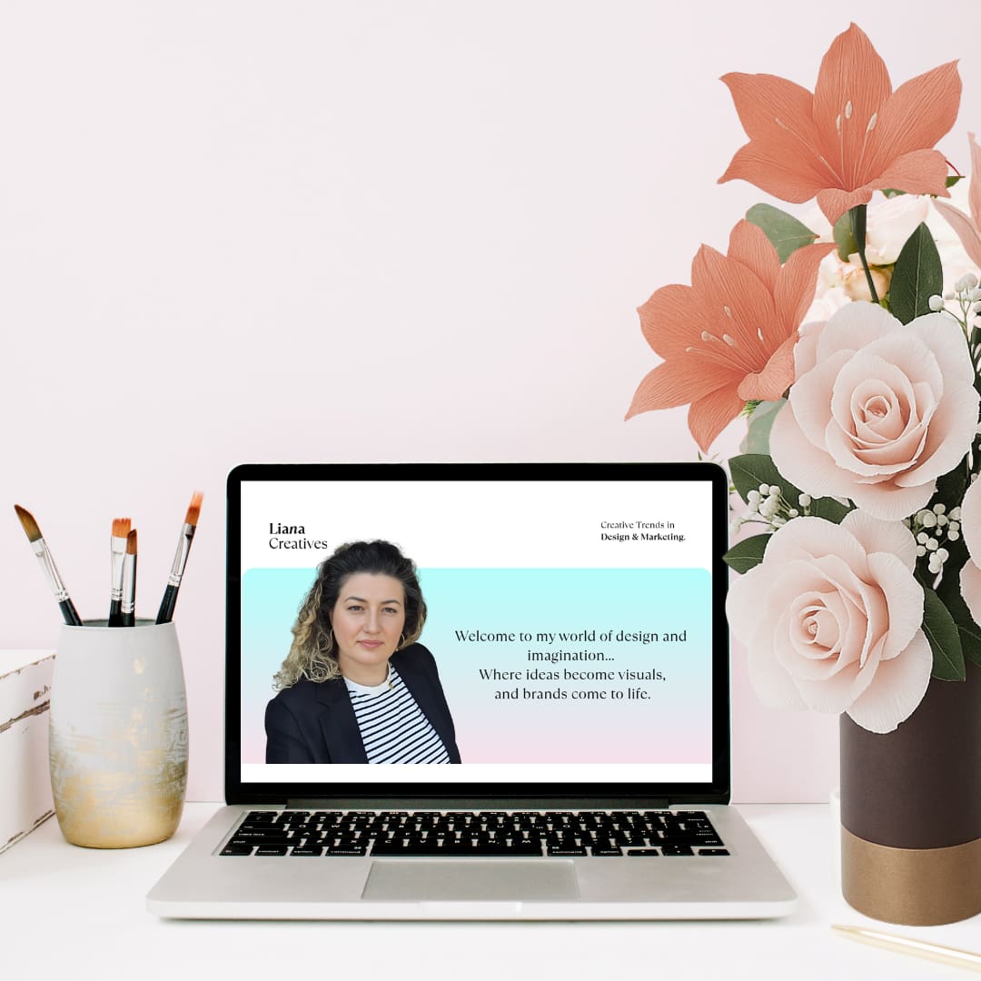 Laptop med Liana Creatives’ designside omgivet af papirroser og koralfarvede papirblomster.